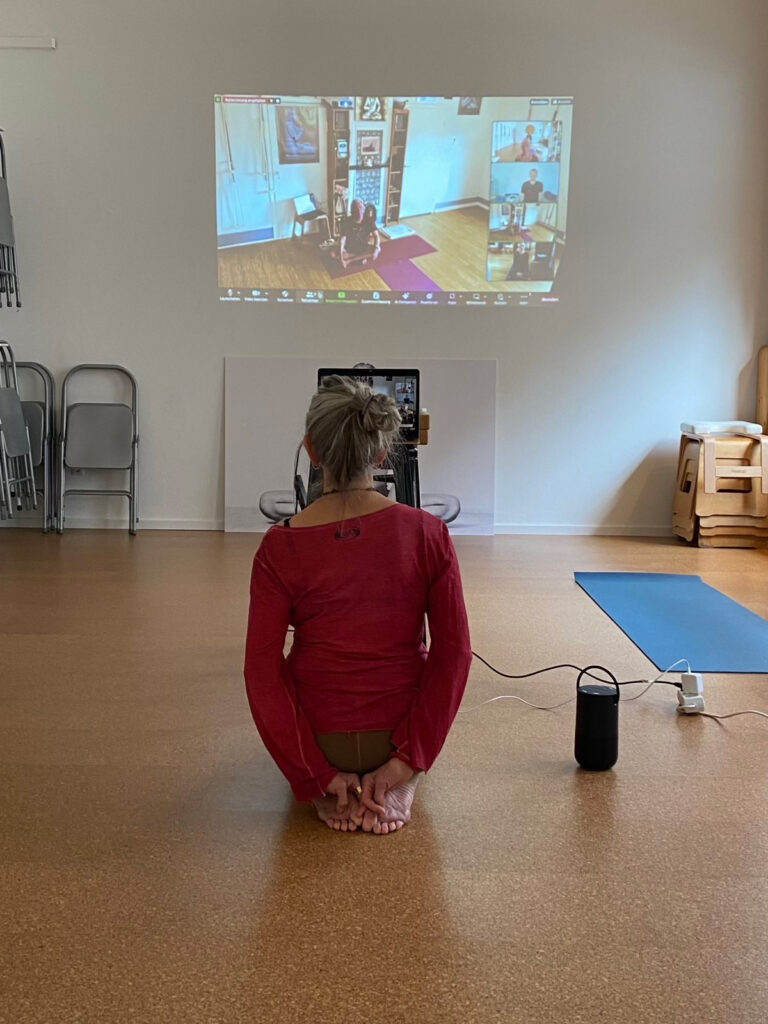 Monika sitzt im Fersensitz im Yogashala und schaut den Jayne-Orten-Workshop auf einem Bildschirm an